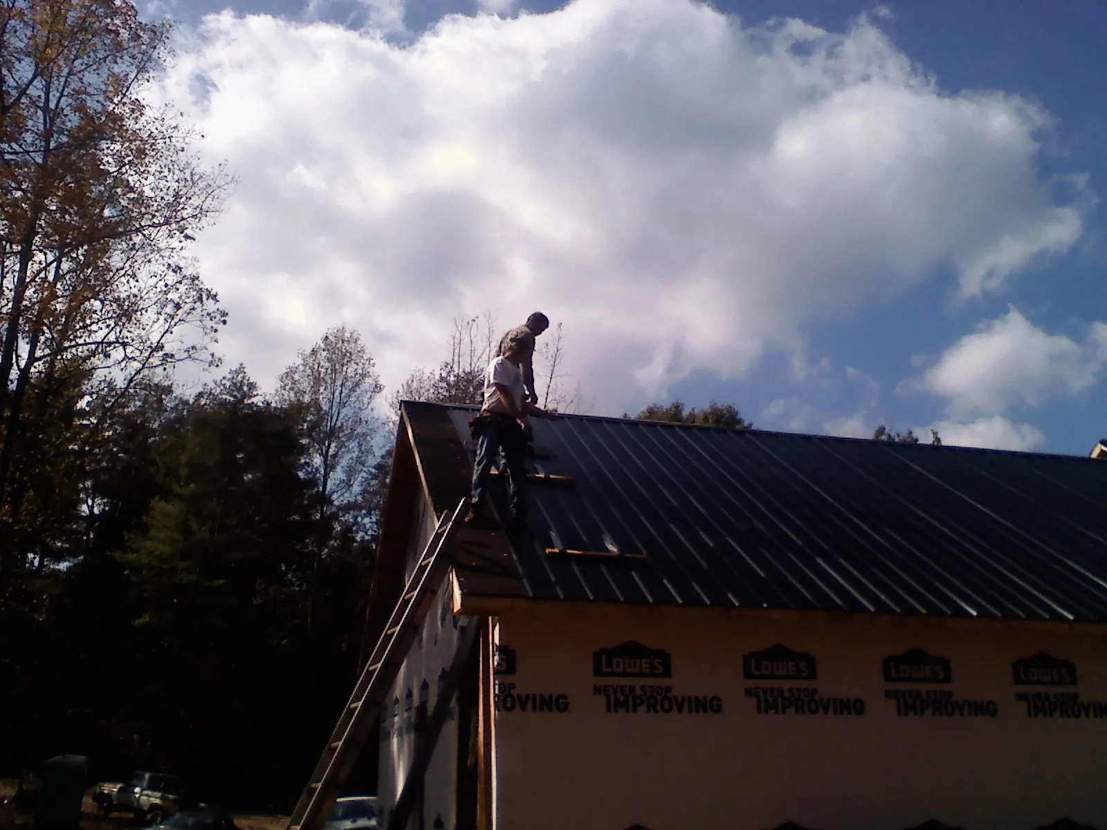 Roofer fastening dark metal panels high against a cloudy sky, from a Roof Inspection job in Hunlock Creek