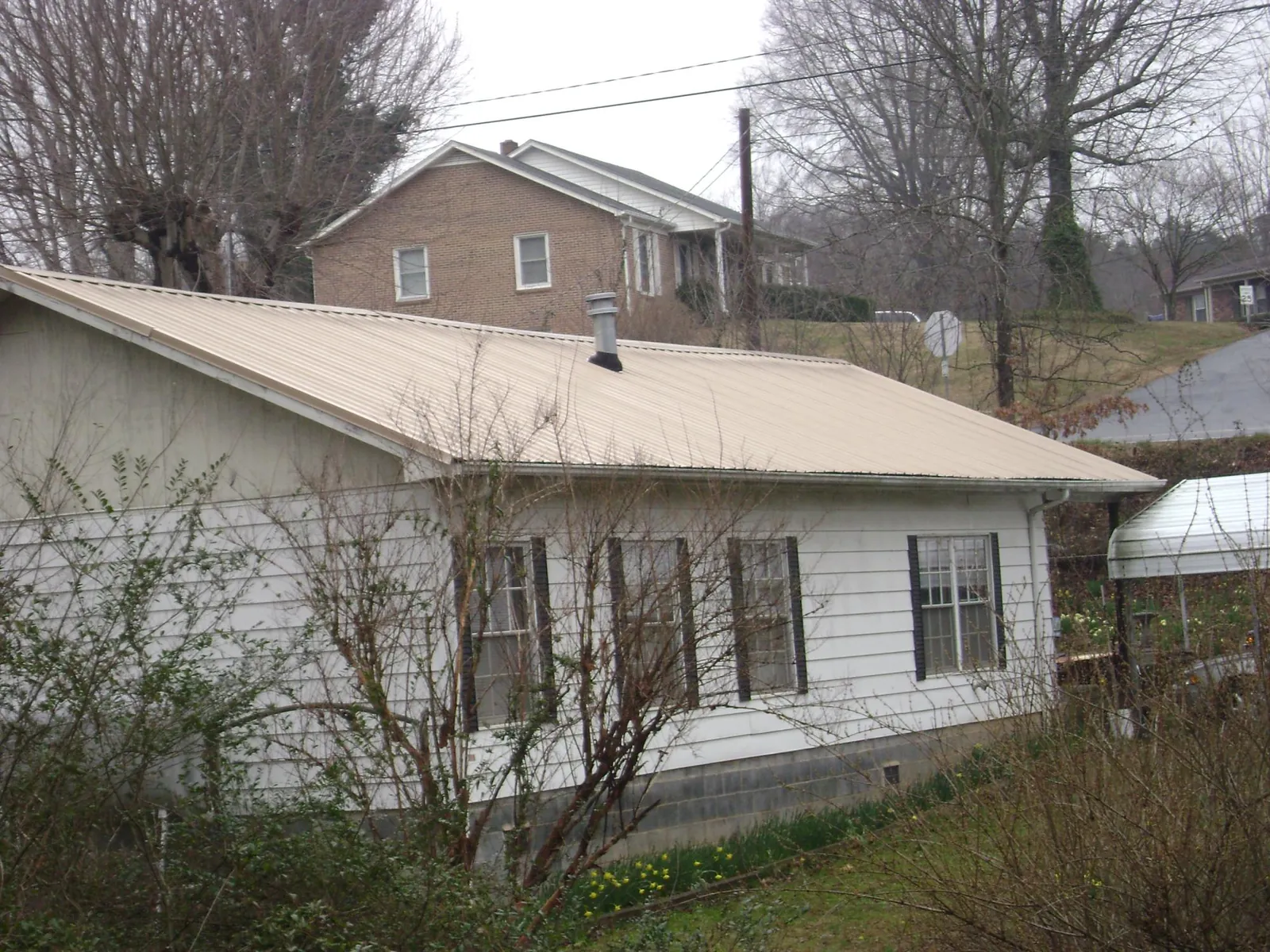 Tan metal roof on a white sided house set into a hillside — Commercial Roofing by Roofing Brothers in Hunlock Creek